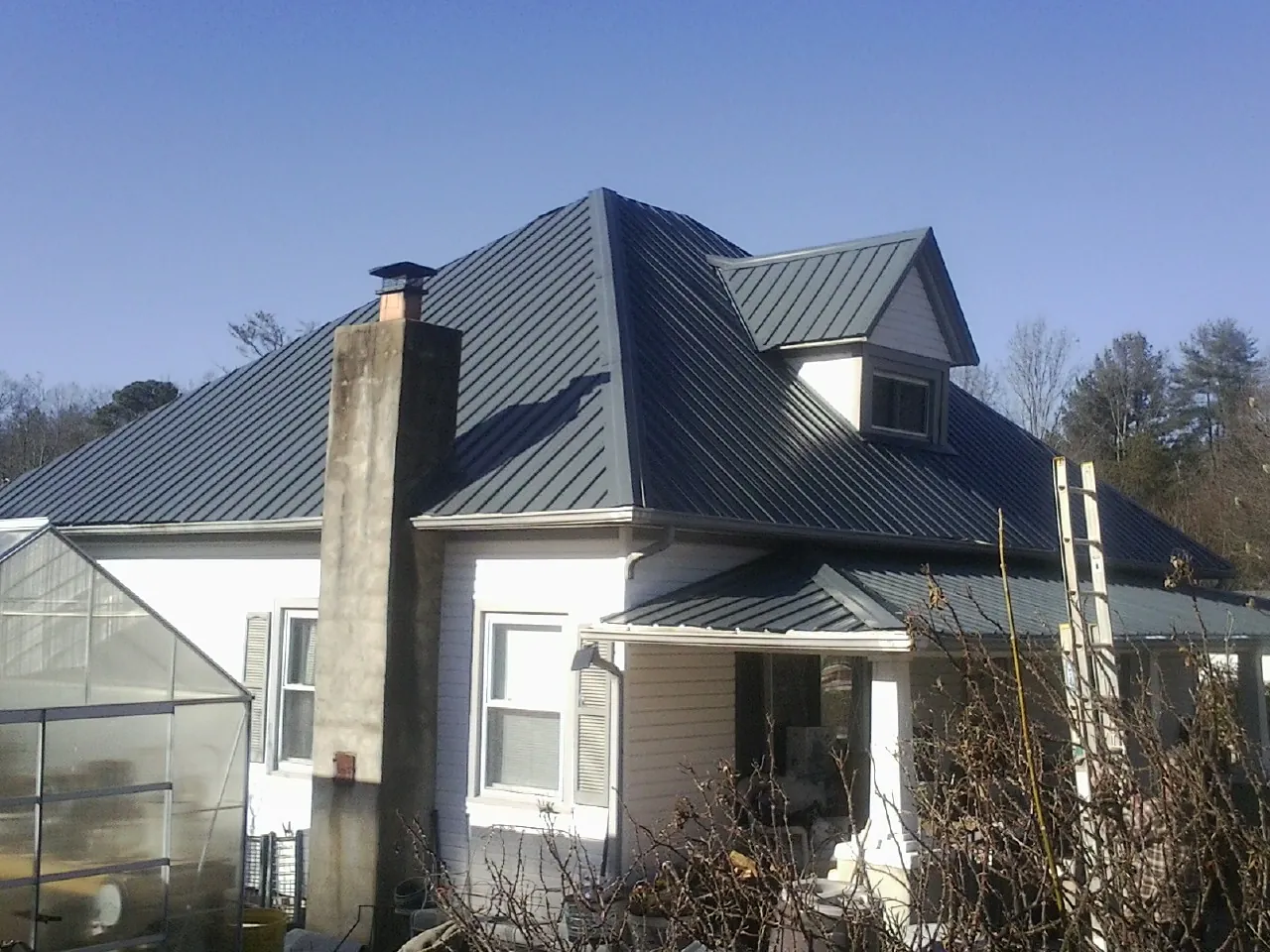 Dark blue standing seam metal roof on a white farmhouse with dormer — Slate & Tile Roof Repair by Roofing Brothers in Dacula