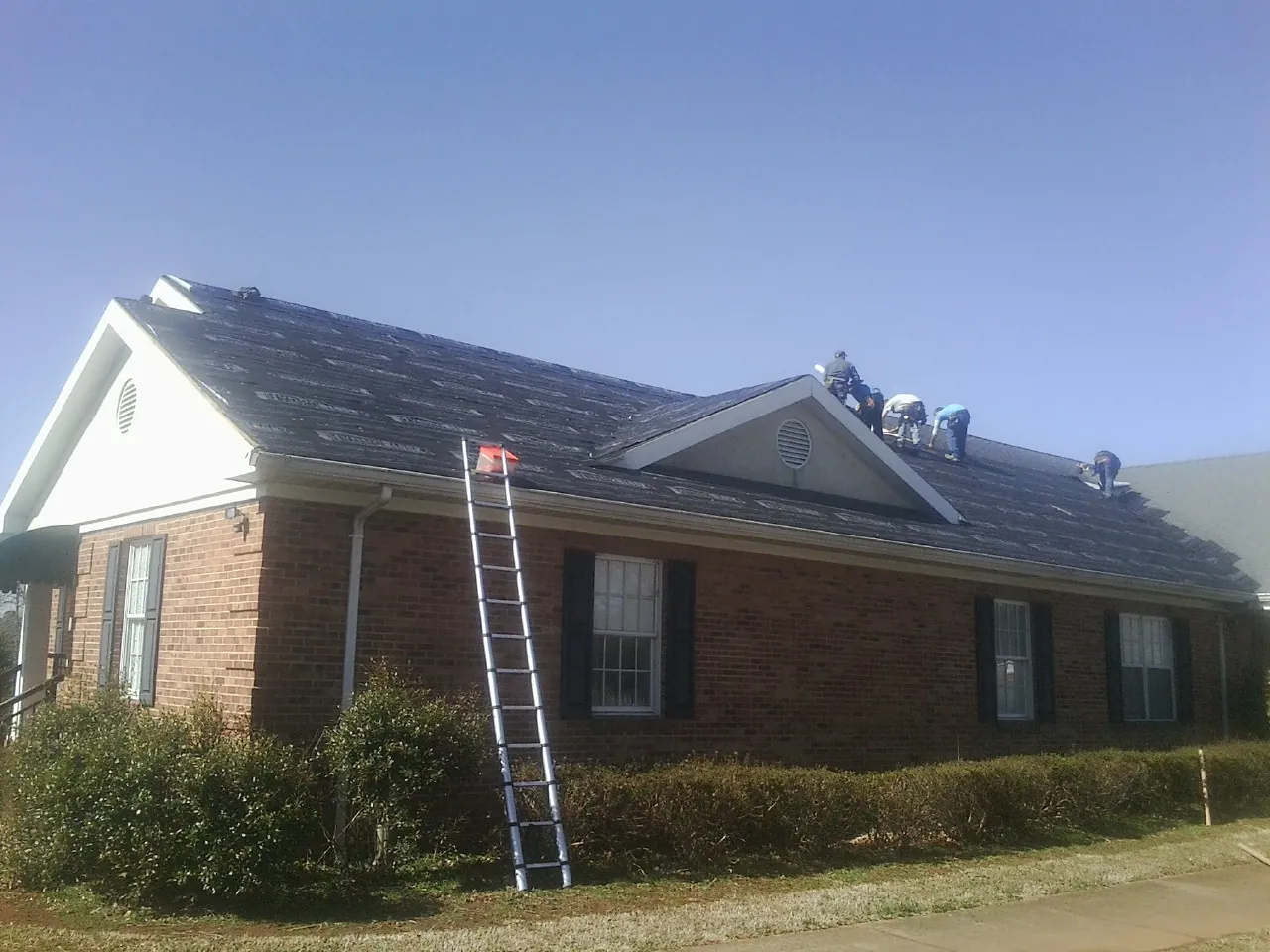 Crew tearing shingles off a brick ranch roof with a ladder set — Emergency Roof Repair work by our crew in Dacula
