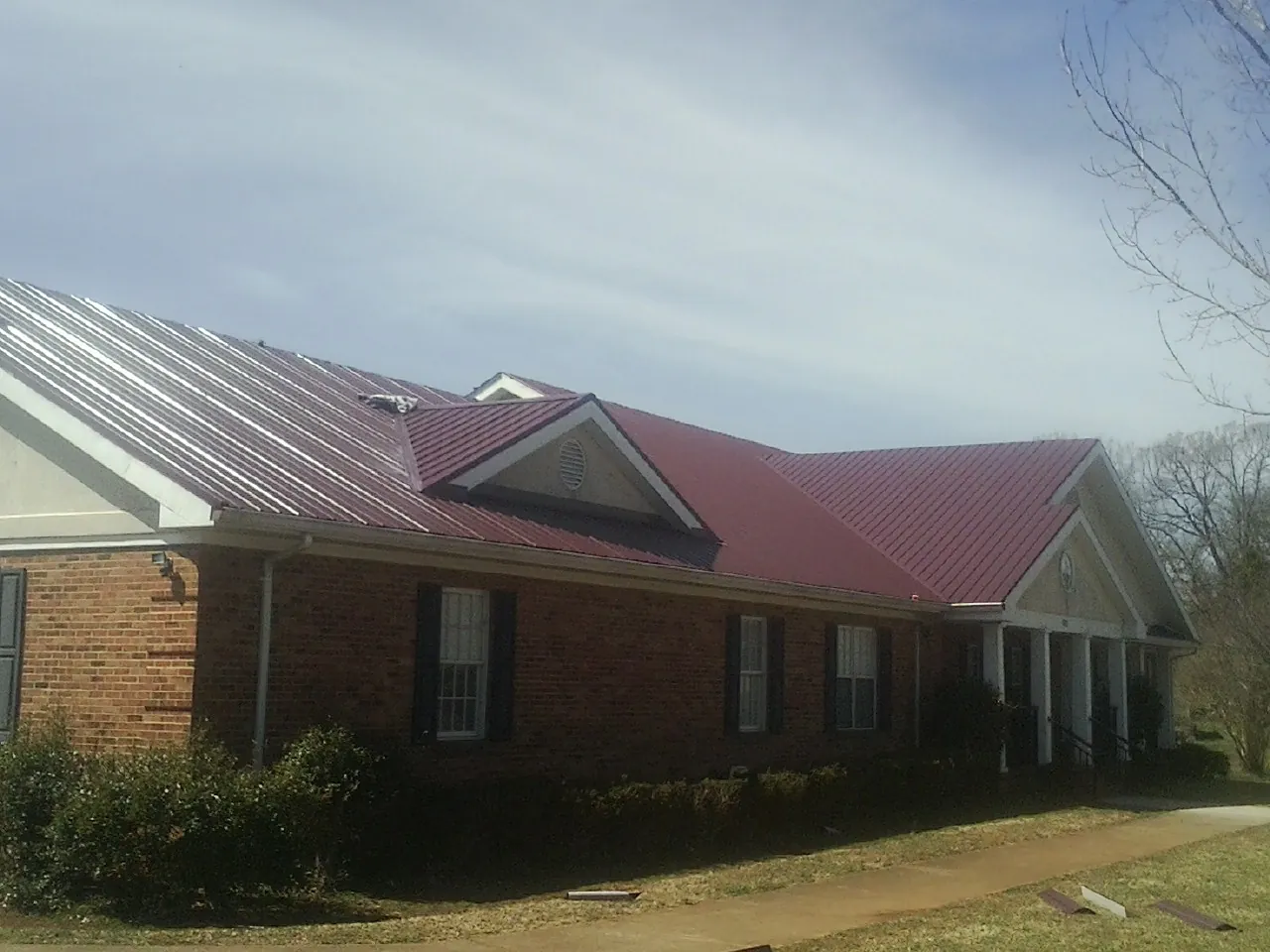 Red metal roof with gabled entries on a long brick building, from a Hail Damage Roof Repair job in Dacula