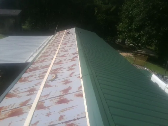 Old rusted panels beside newly installed green metal roofing — Wind Damage Roof Repair by Roofing Brothers in Dacula
