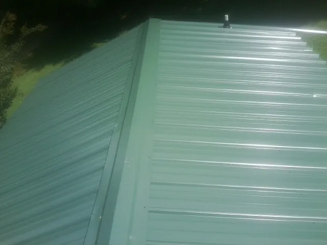 New green metal panels meeting at the ridge of a roof — Flat Roof Repair work by our crew in Dacula