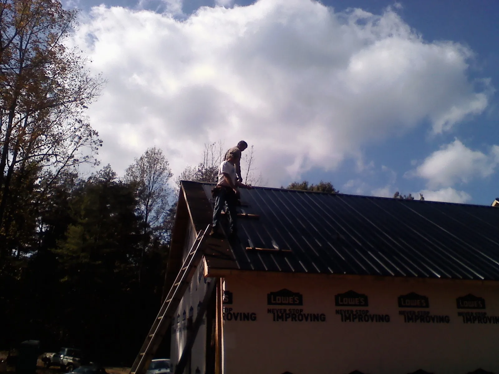 Roofer fastening dark metal panels high against a cloudy sky, from a Roof Inspection job in Dacula