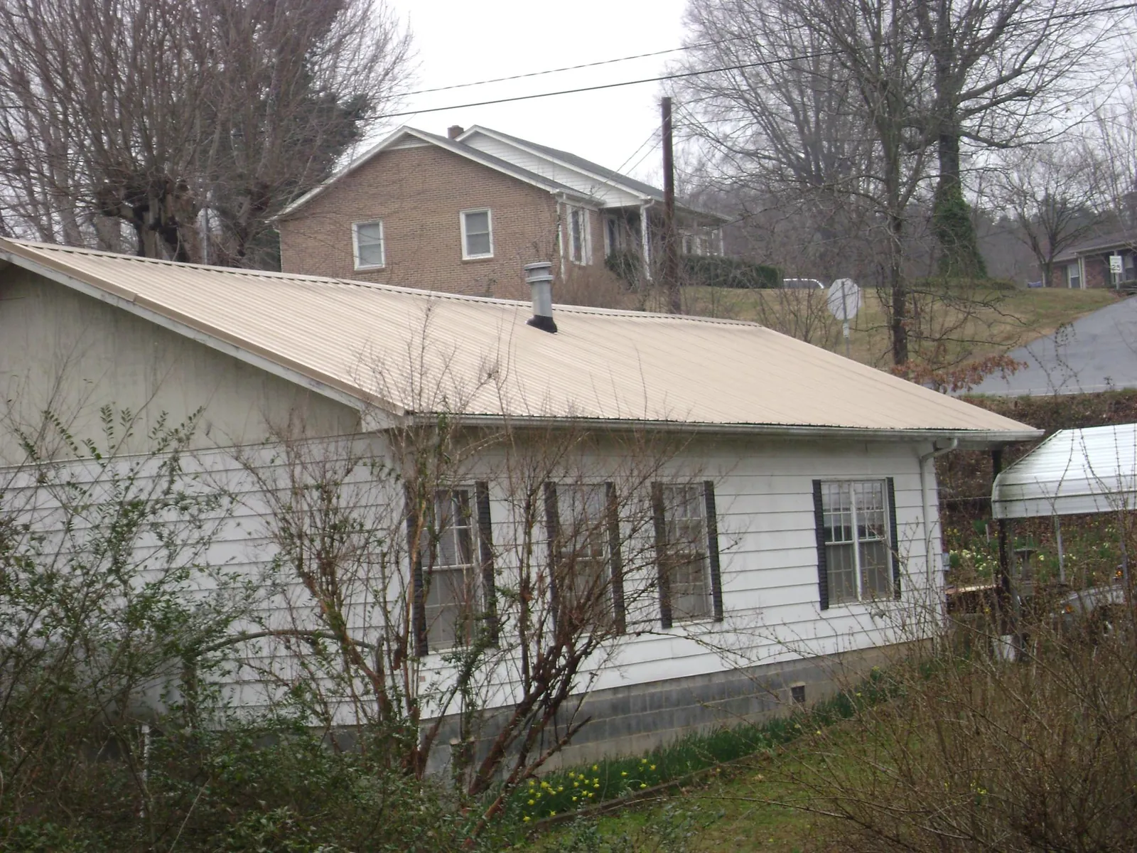 Tan metal roof on a white sided house set into a hillside — Commercial Roofing by Roofing Brothers in Dacula